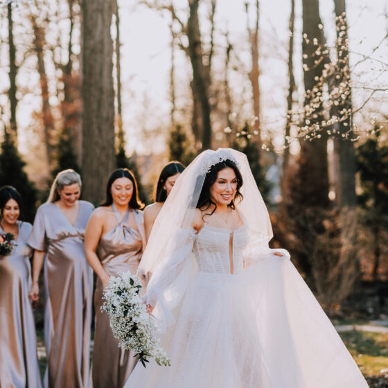 Bride smiles as she walks in front of bridal party in garden.