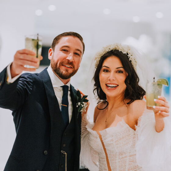 Bride and groom raise their cocktail glasses and smile for photo.
