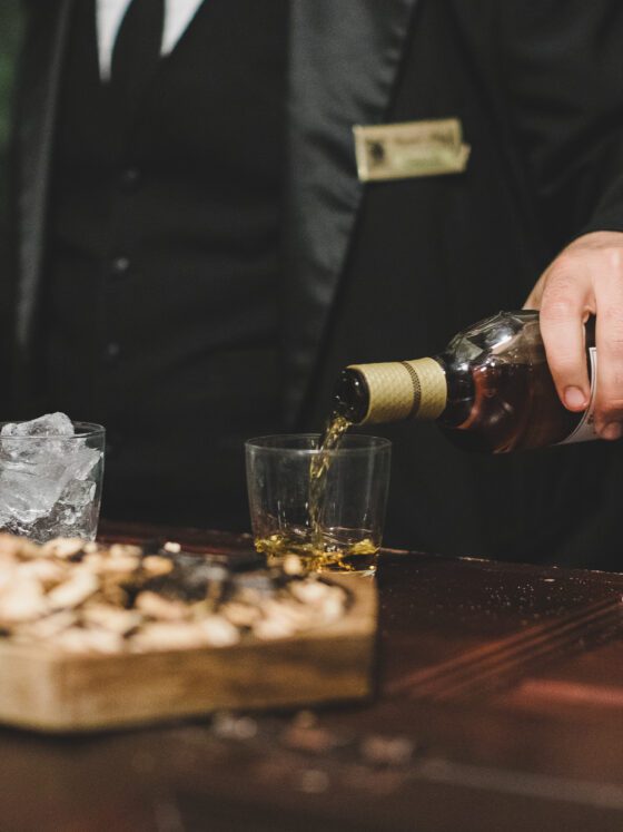 Mixologist pours bourbon into a rocks glass.