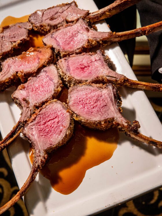 Sliced rack of lamb, perfectly cooked and displayed on white platter.