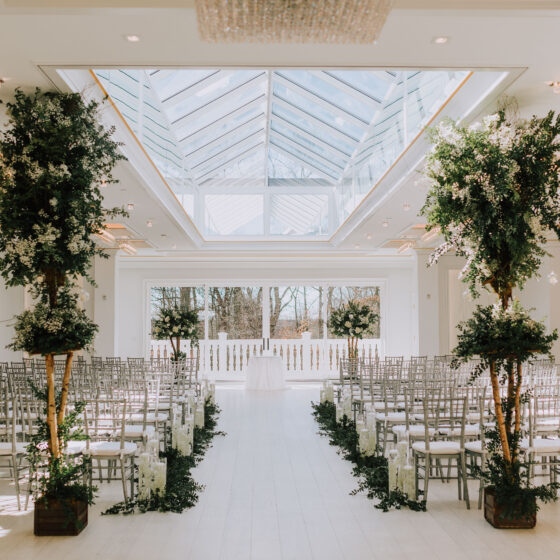 Crystal Plaza's Atrium is decorated in simple greenery displays, white flowers, silver chairs, and candles.