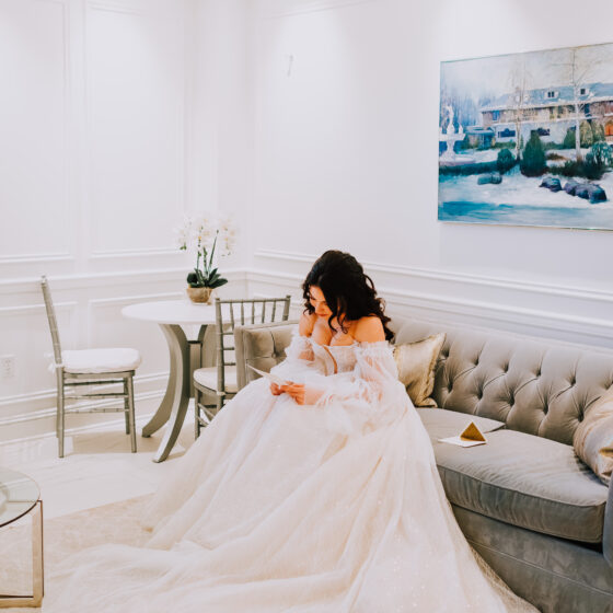 Bride sits on couch and reads note from her groom before ceremony.