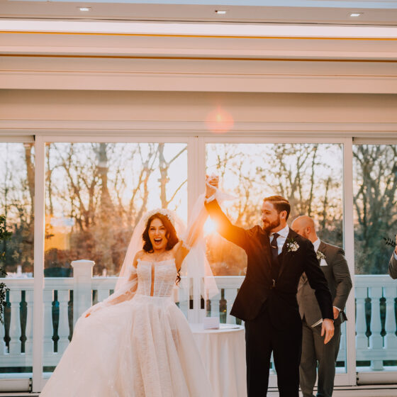 Bride and groom raise their hands and smile as a just married couple.