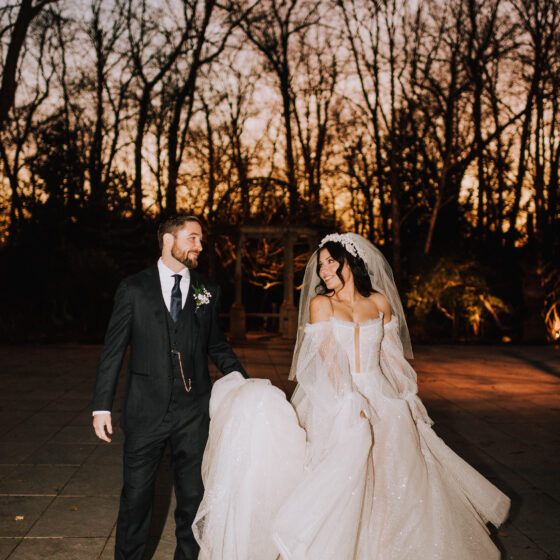 Groom holds brides dress as they walk through Crystal Plaza's garden during winter.