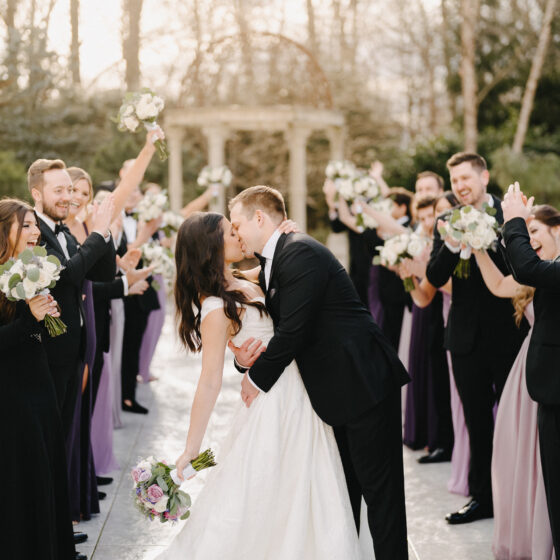 Groom kisses bride as bridal party cheers in Crystal Plaza's garden.
