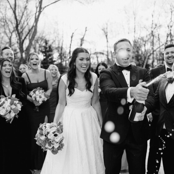 Groom pops champagne as bride, groomsmen, and bridesmaids cheer in Crystal Plaza's garden.