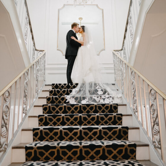 Bride and groom kiss at the top of a grand staircase.