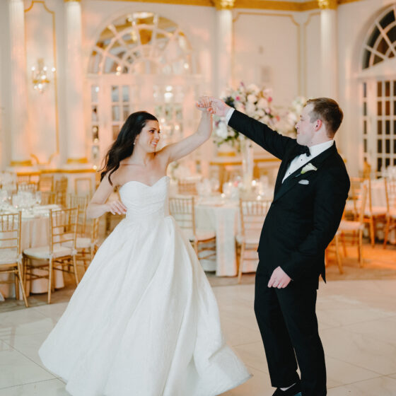 Groom twirls bride on dance floor.