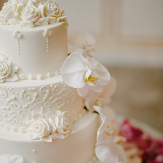 Simple buttercream frosted wedding cake with delicate pipping and white orchid flowers.