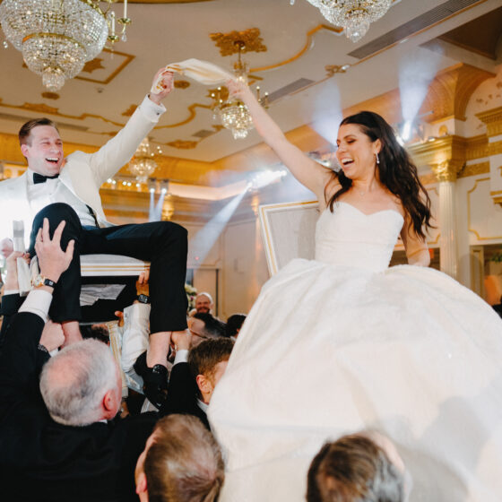 Bride and groom are lifted up on chairs above guests on the dance floor.