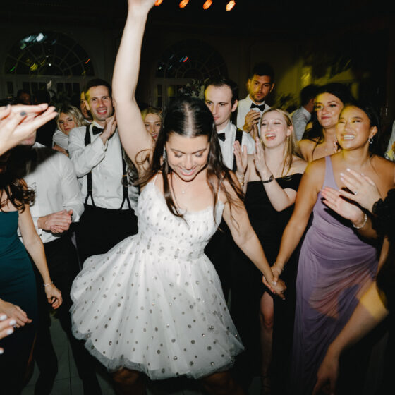 Bride dances with enthusiasm as guests gather round and cheer her on.