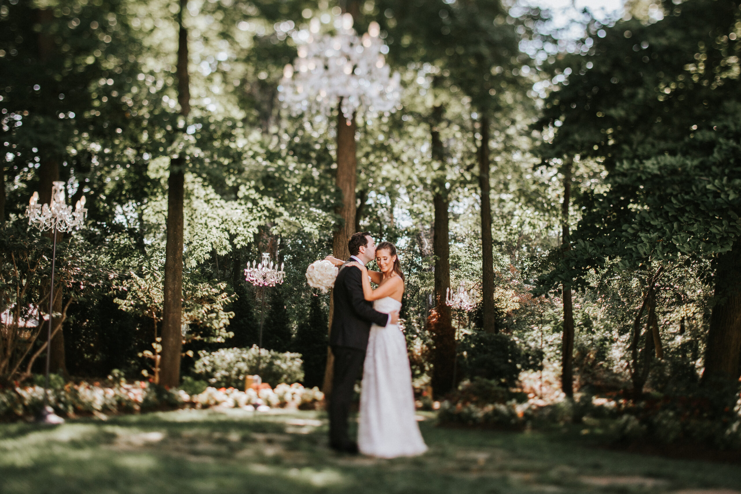 Groom kisses bride in Crystal Plaza's well-manicured gardens, filled with lush greenery, trees, and flowers.