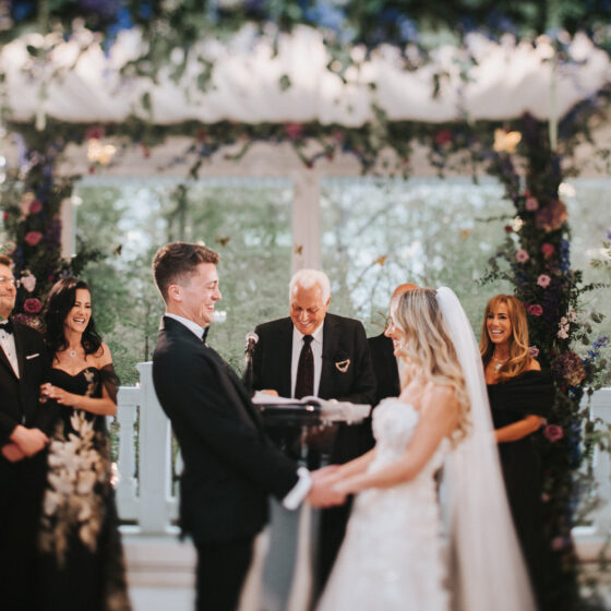 Bride and groom hold hands and smile as a just married couple underneath a stunning floral chuppah in Crystal Plaza's Atrium.