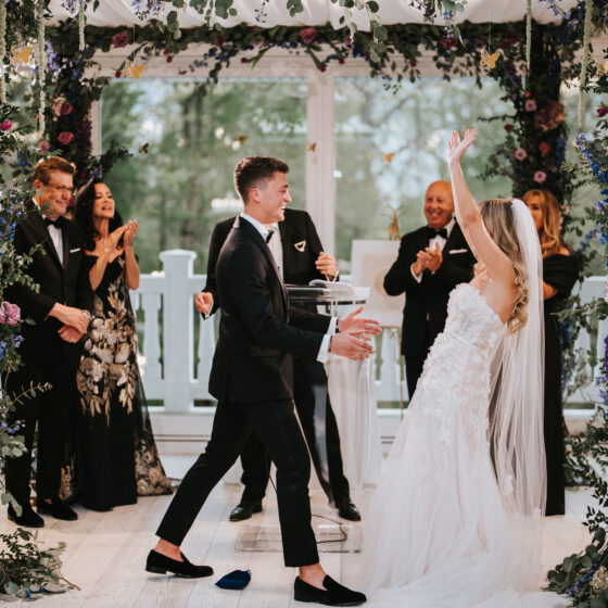 Bride and groom celebrate as a just married couple underneath a stunning floral chuppah in Crystal Plaza's Atrium.