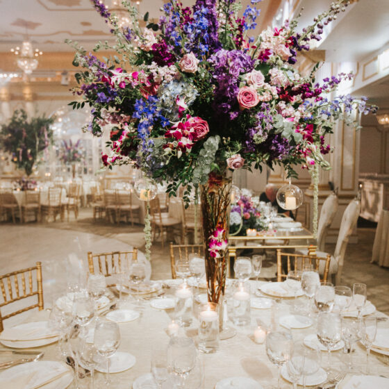 Colorful wedding reception centerpiece filled with pink, blue, purple, and red flowers and greenery.
