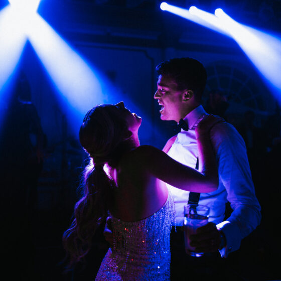Bride and groom dancing at the wedding after party as they're illuminated by dark blue lights.