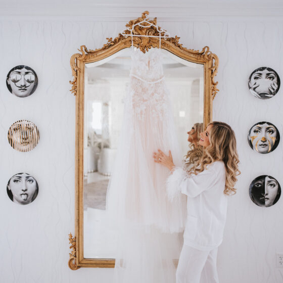 Bride admires bridal gown hanging from large gold mirror in Crystal Plaza's Penthouse Suite.