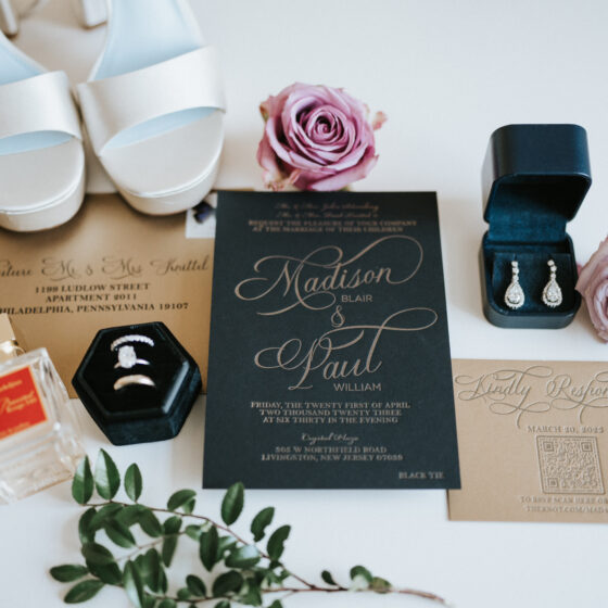 Overview of wedding invitations with perfume, earrings, wedding bands, and silver heels.