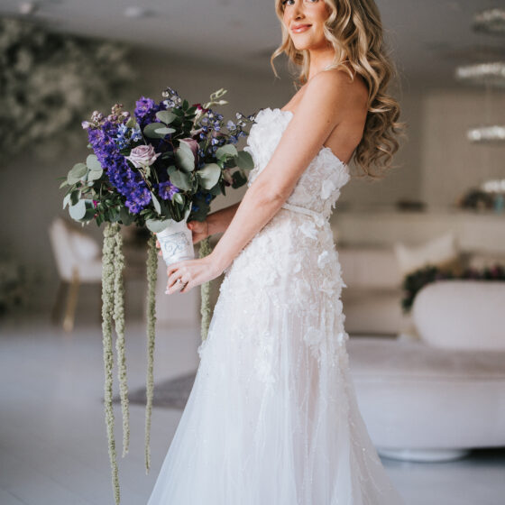 Bride poses for wedding portrait holding lush purple bouquet of flowers in Crystal Plaza's Penthouse Suite.