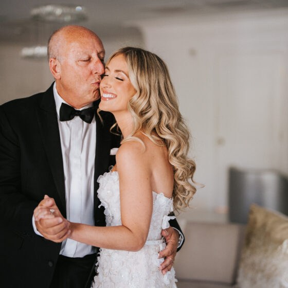 Father of the bride kisses daughter on cheek in Crystal Plaza's Penthouse Suite.
