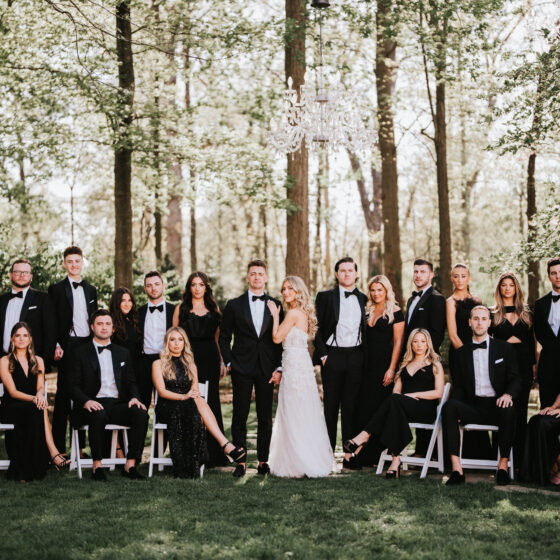 Bride and groom pose for wedding photo with groomsmen and bridal party in black tie attire.