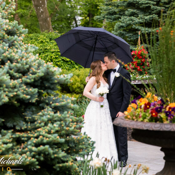 Spring wedding photography of bride and groom holding umbrella in Crystal Plaza's garden.