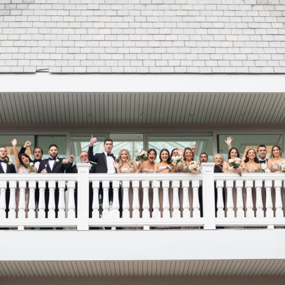 Wedding party stands on balcony watching bride and groom first look.
