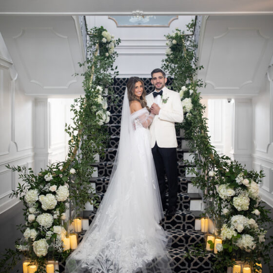 Bride and groom pose on staircase surrounded by lush greenery.