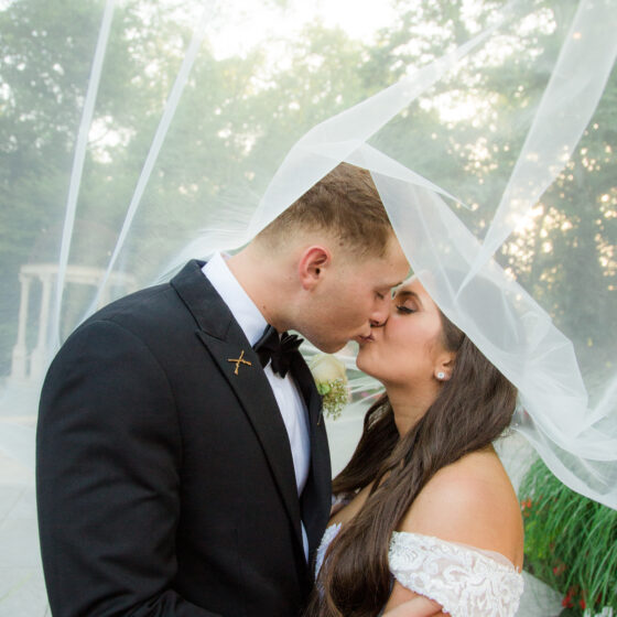 Bride and groom kiss underneath bride's veil.