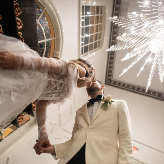 Bride and groom kiss underneath elegant crystal chandelier.