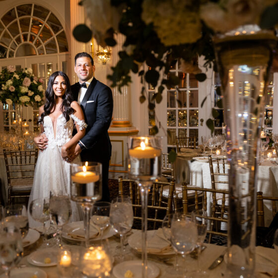 Bride and groom pose amongst elegant table settings in Crystal Plaza's grand ballroom.