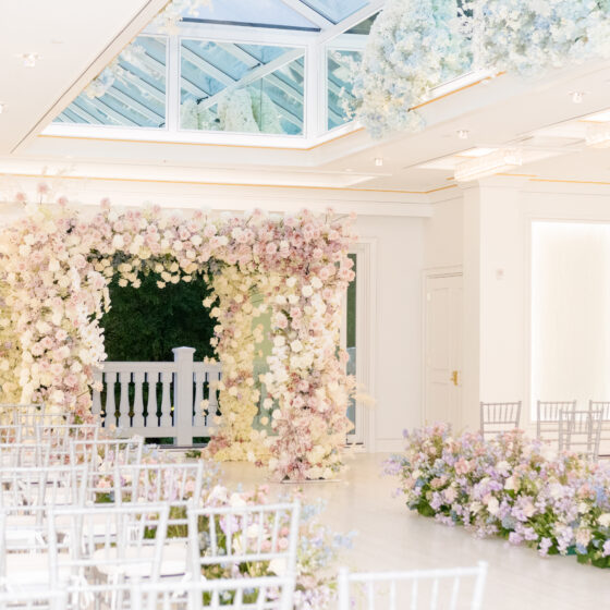 Spring flower arch in the Atrium filled with light pink and white roses. Aisle lined with pastel purple and blue flowers.