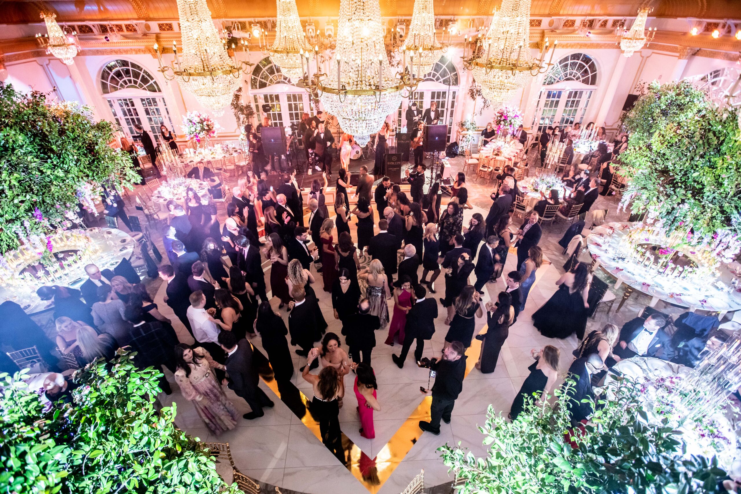 Guests mingle in Crystal Plaza's Grand Ballroom adorned with chandeliers, tree centerpieces, and purple flower accents.