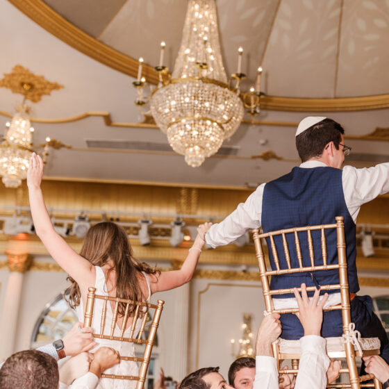 Bride and groom are lifted in chairs above wedding guests on dance floor.