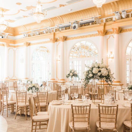 Elegant wedding reception decor with gold accents, white table clothes, and white floral centerpieces.