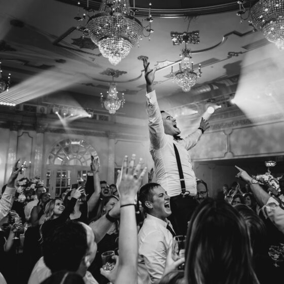 Groom is lifted above crowd with his arms up on the dance floor in Crystal Plaza's grand ballroom.