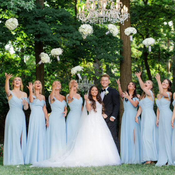 Bride and groom pose for wedding portrait as bridal party throws their white bouquets in the air.