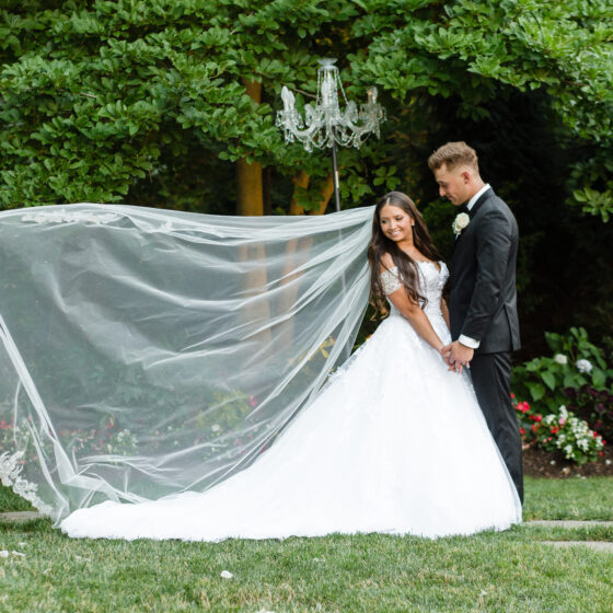 Bride and groom pose for wedding portrait as her veil lifts effortlessly in the breeze.