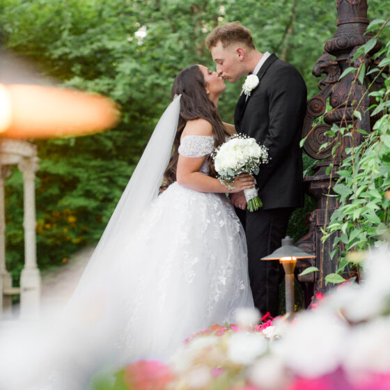 Bride and groom kiss in romantic garden setting.