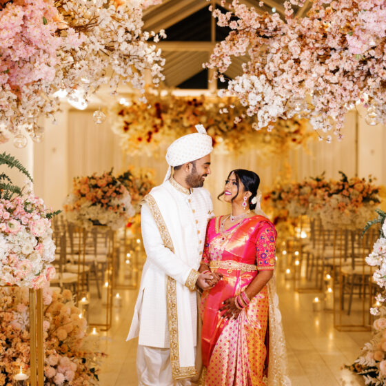 Bride and groom pose for photo amongst beautiful pink and white flowers, decorated elegantly throughout Crystal Plaza's Atrium.