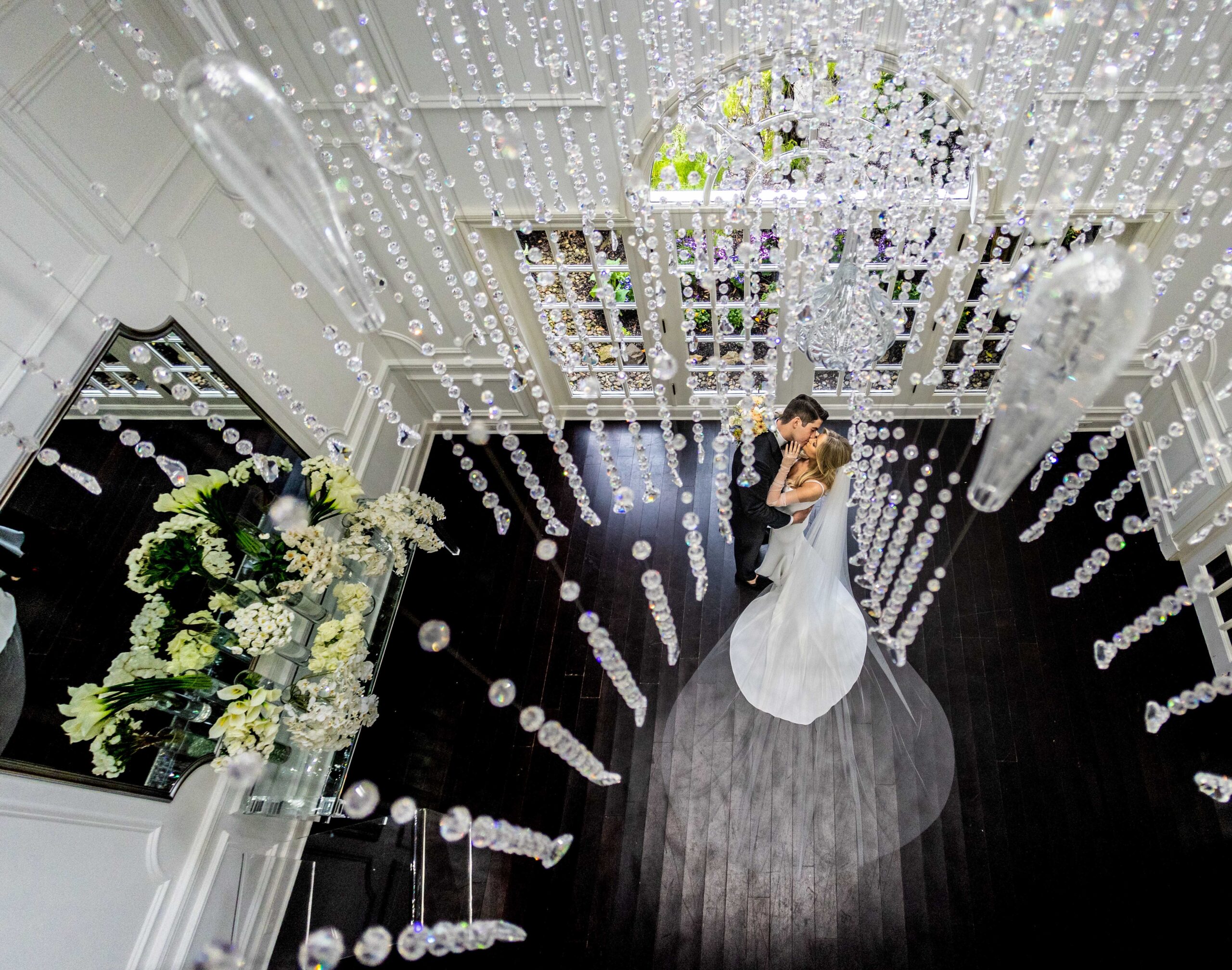 Bride and groom kiss in the foyer of Crystal Plaza under a crystal chandelier.