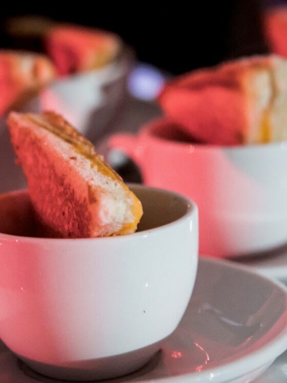 Mini grilled cheeses in saucer cups filled with tomato soup.