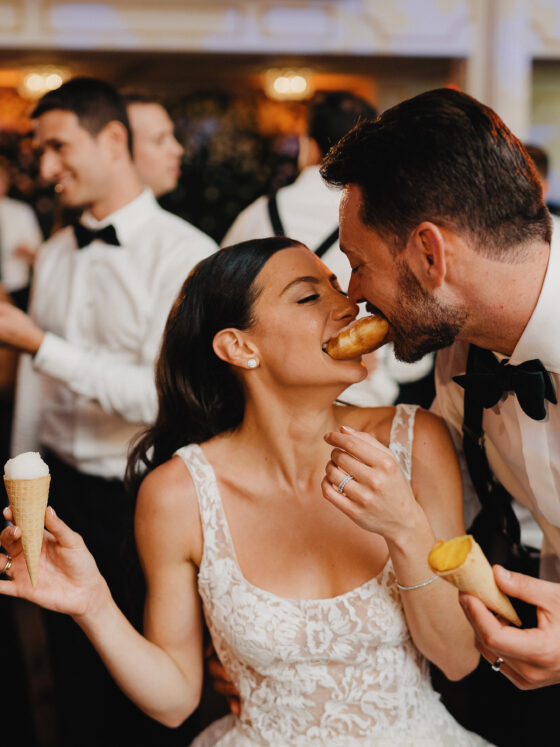 Bride and groom share donut at wedding reception.